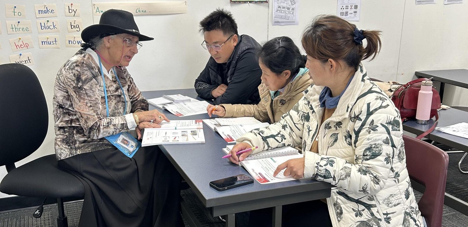 An instructor supports three adult learners with English exercises