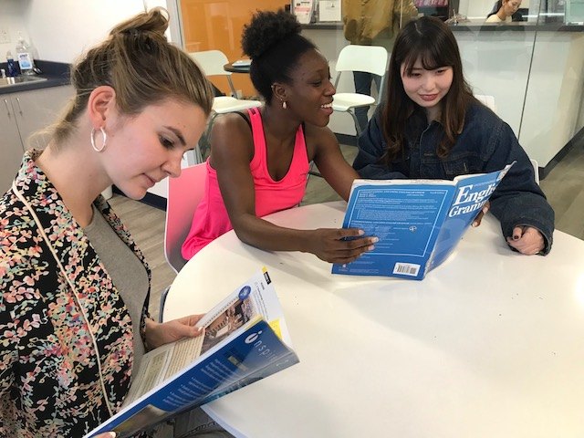 Three learners discuss English study materials around a table