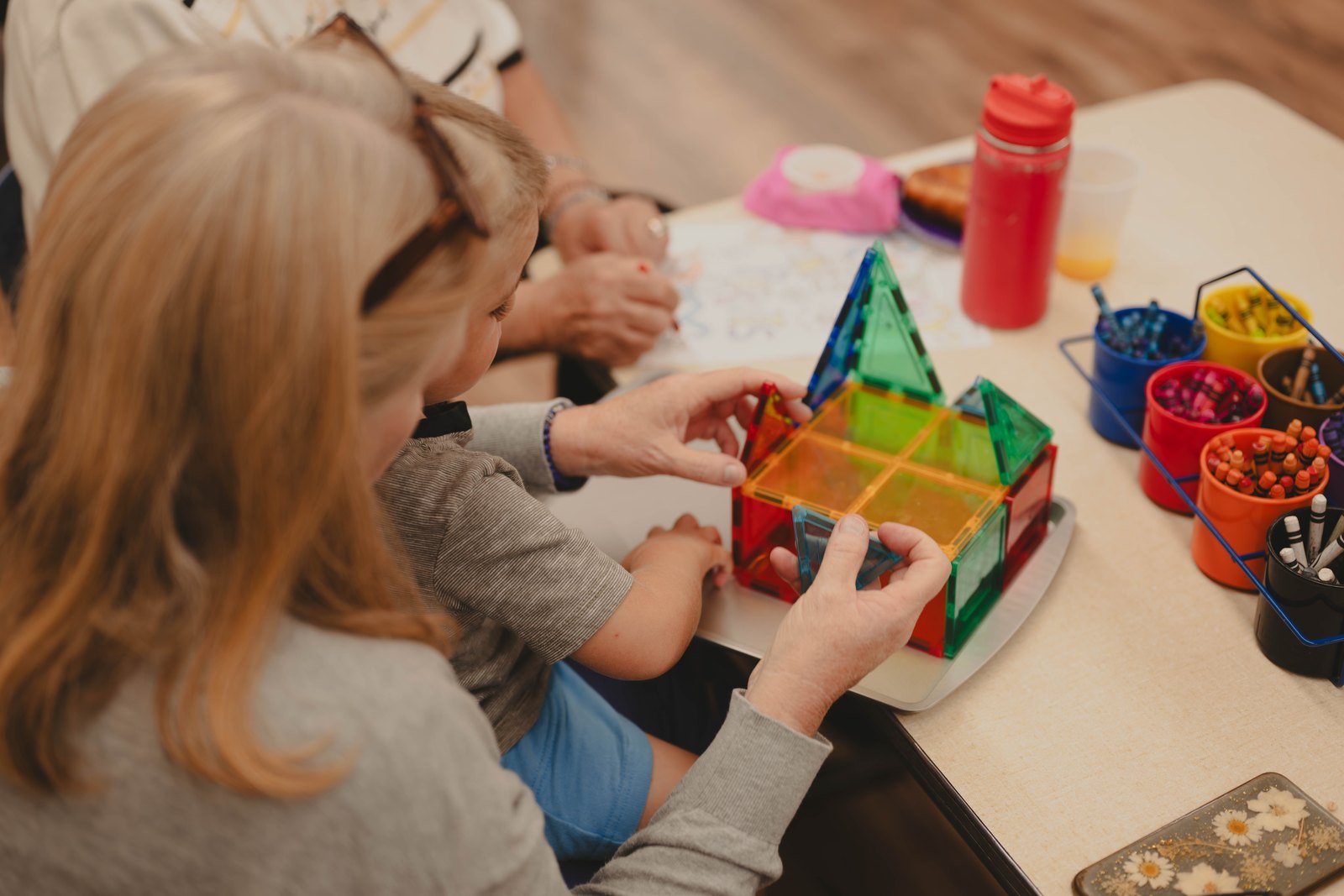 A child builds shapes with magnetic tiles alongside an adult